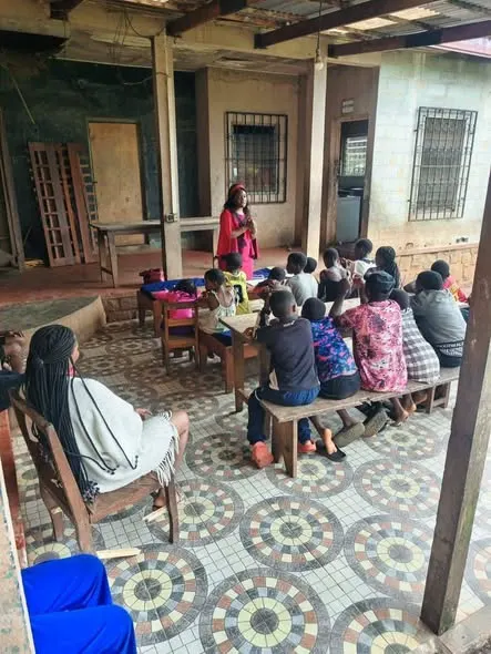 Children seated on benches on a veranda listening to the facilitator at the orphanage