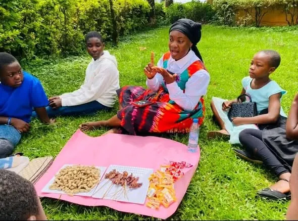 A facilitator in a Toghu-patterned top leading a discussion with girls seated on the grass